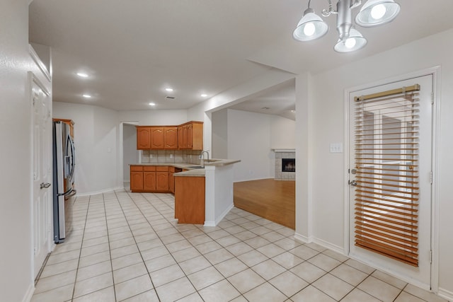 kitchen featuring light tile patterned flooring, decorative light fixtures, stainless steel refrigerator, kitchen peninsula, and decorative backsplash