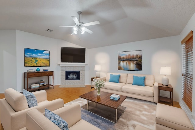 living room featuring a tile fireplace, ceiling fan, wood-type flooring, a textured ceiling, and vaulted ceiling