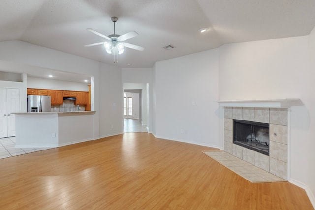 unfurnished living room with ceiling fan, a fireplace, vaulted ceiling, and light wood-type flooring