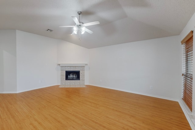 unfurnished living room with lofted ceiling, a tile fireplace, ceiling fan, light hardwood / wood-style floors, and a textured ceiling