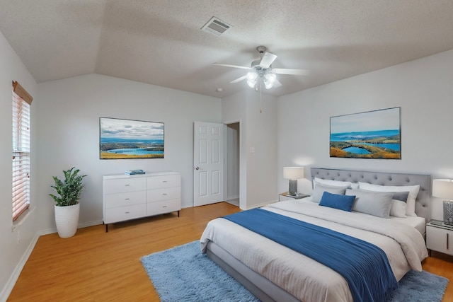 bedroom with ceiling fan, vaulted ceiling, light hardwood / wood-style floors, and a textured ceiling