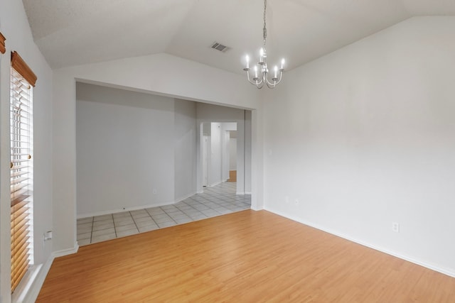 empty room featuring a notable chandelier, vaulted ceiling, and light wood-type flooring