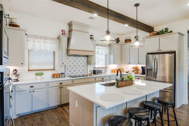 kitchen featuring pendant lighting, sink, appliances with stainless steel finishes, custom range hood, and an island with sink