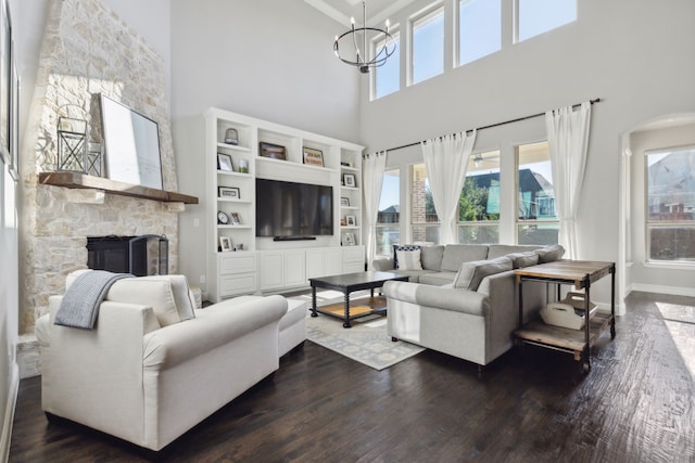 living area featuring baseboards, a chandelier, dark wood finished floors, and a stone fireplace