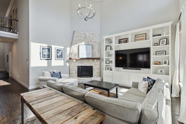 living room with baseboards, wood finished floors, a high ceiling, a stone fireplace, and a chandelier