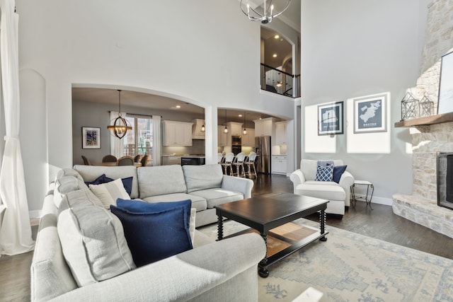 living room featuring dark wood-style flooring, a fireplace, a notable chandelier, a towering ceiling, and baseboards