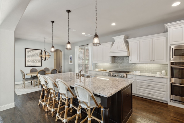 kitchen with arched walkways, stainless steel appliances, custom range hood, decorative backsplash, and a sink