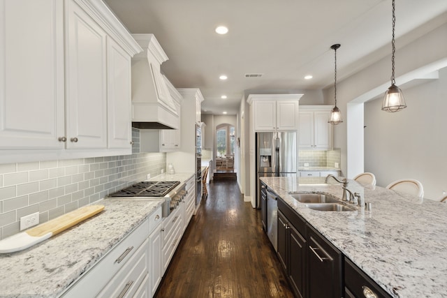 kitchen featuring arched walkways, stainless steel appliances, visible vents, custom range hood, and a sink