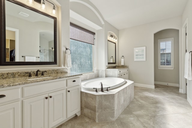 bathroom featuring a garden tub, two vanities, a sink, visible vents, and baseboards