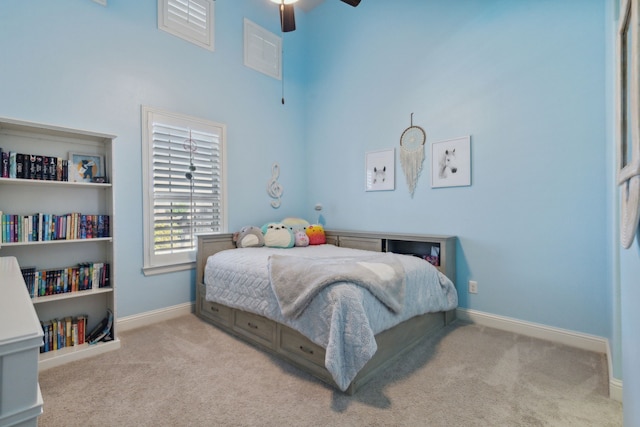 carpeted bedroom with a high ceiling, a ceiling fan, and baseboards