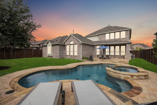 back of property at dusk with a fenced backyard, a yard, a patio area, a pool with connected hot tub, and brick siding