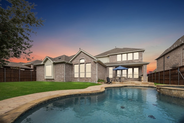 back of property at dusk with a yard, brick siding, a patio, and fence