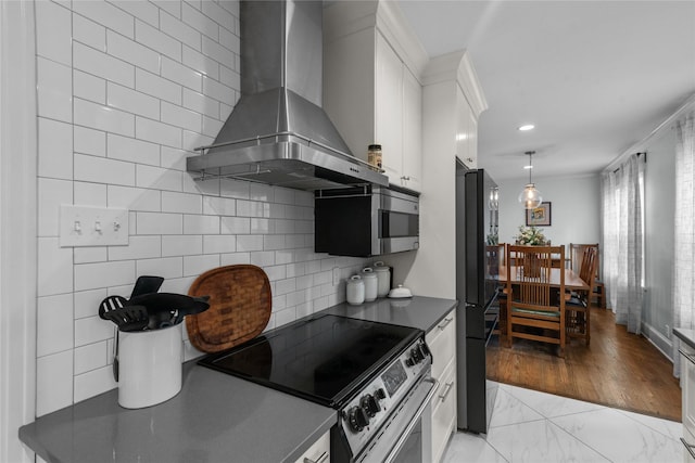 kitchen featuring appliances with stainless steel finishes, decorative light fixtures, white cabinets, decorative backsplash, and wall chimney exhaust hood