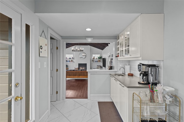 kitchen with sink, vaulted ceiling, a large fireplace, white cabinets, and backsplash