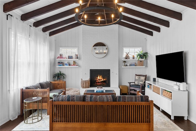 living room featuring lofted ceiling with beams, wood-type flooring, a brick fireplace, and an inviting chandelier