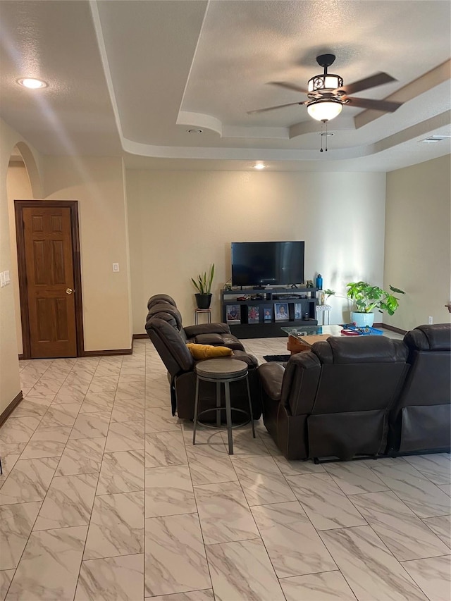 living room with a tray ceiling, a textured ceiling, and ceiling fan