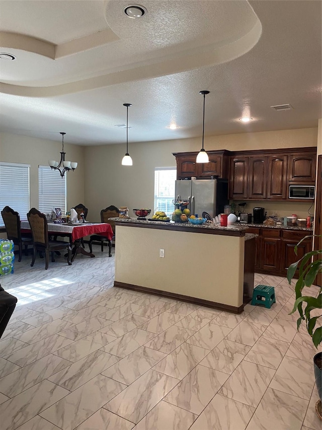 kitchen featuring hanging light fixtures, black microwave, dark brown cabinetry, an island with sink, and stainless steel fridge with ice dispenser