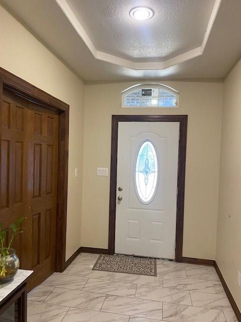 foyer entrance featuring a raised ceiling and a textured ceiling