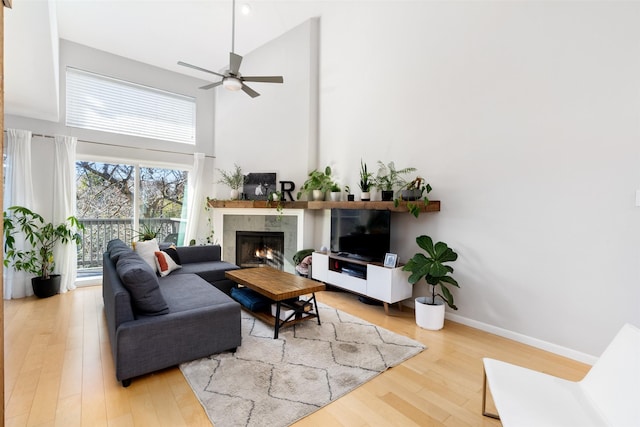 living room with hardwood / wood-style flooring, a tile fireplace, ceiling fan, and a towering ceiling