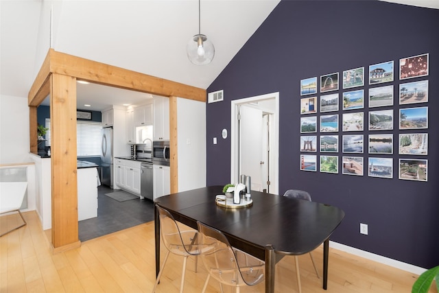 dining space featuring sink, high vaulted ceiling, and light hardwood / wood-style flooring