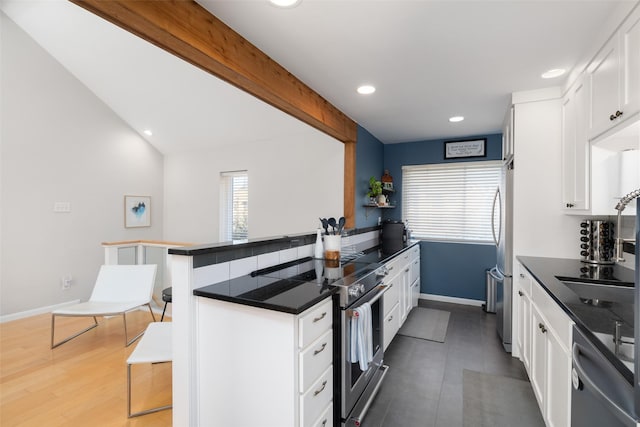 kitchen with a breakfast bar, white cabinetry, stainless steel appliances, lofted ceiling with beams, and kitchen peninsula