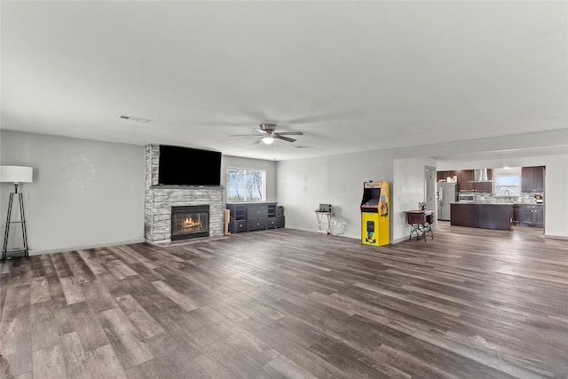 unfurnished living room with wood-type flooring, a stone fireplace, and ceiling fan