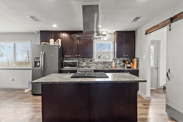 kitchen featuring stainless steel refrigerator with ice dispenser, island range hood, dark stone countertops, a kitchen island, and a barn door