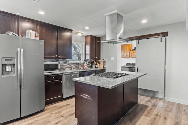 kitchen with appliances with stainless steel finishes, island range hood, a center island, a barn door, and dark brown cabinets