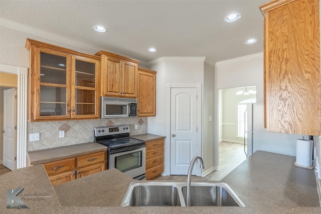 kitchen with sink, a textured ceiling, ornamental molding, stainless steel appliances, and backsplash