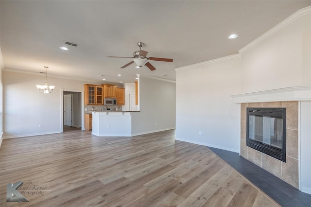 unfurnished living room featuring a tiled fireplace, hardwood / wood-style floors, ceiling fan with notable chandelier, and ornamental molding