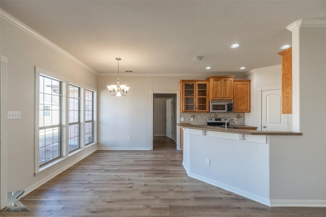 kitchen with appliances with stainless steel finishes, hanging light fixtures, a notable chandelier, kitchen peninsula, and light wood-type flooring