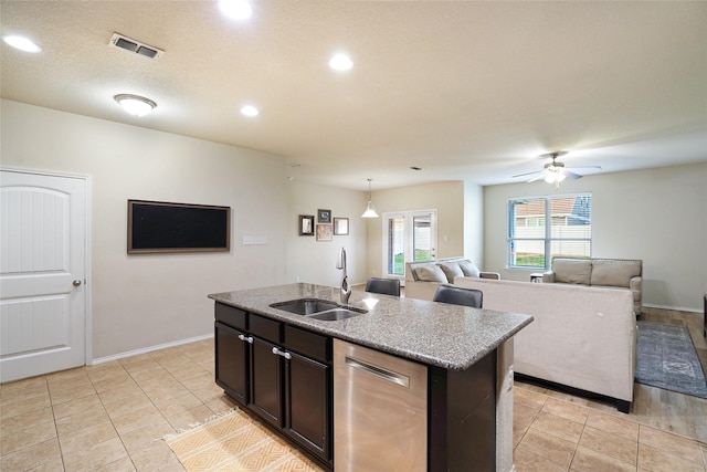 kitchen with decorative light fixtures, dishwasher, sink, light stone countertops, and a center island with sink