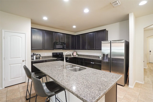 kitchen with sink, light stone counters, a center island with sink, light tile patterned floors, and black appliances