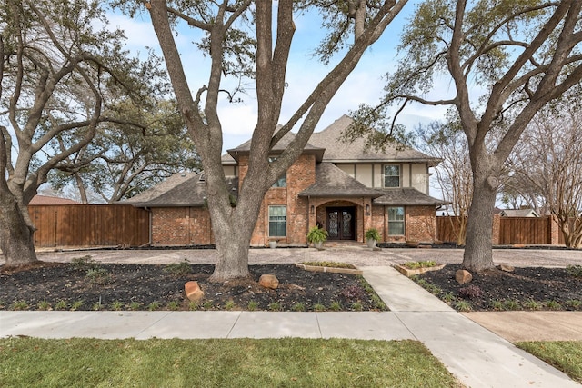 traditional home featuring brick siding, roof with shingles, and fence