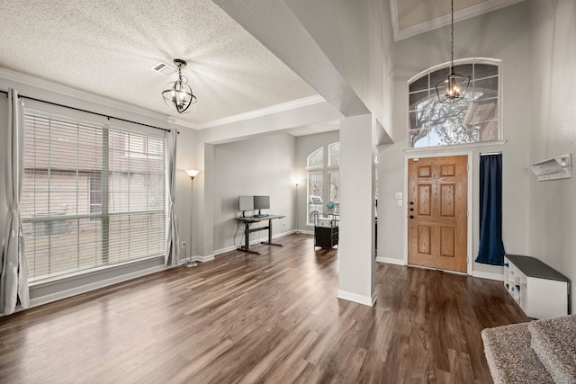 entryway featuring dark wood-type flooring, an inviting chandelier, crown molding, a textured ceiling, and a wealth of natural light