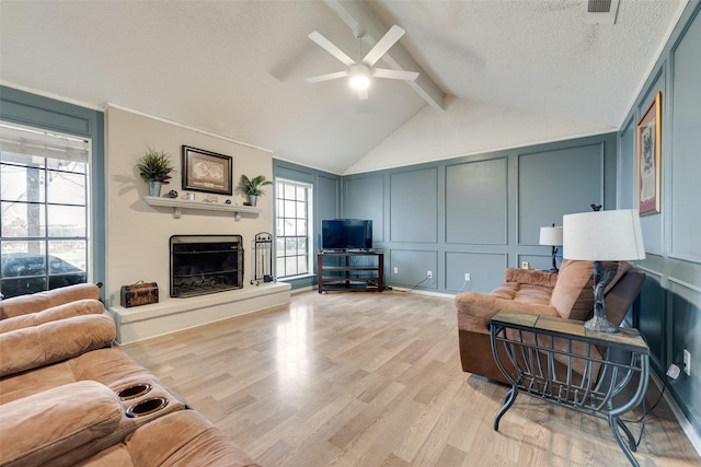 living room featuring lofted ceiling with beams, ceiling fan, a textured ceiling, and light wood-type flooring