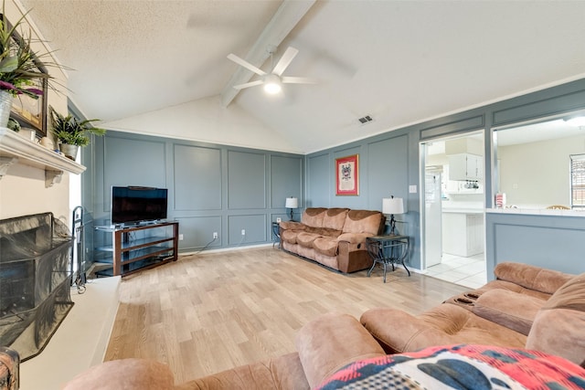 living room with ceiling fan, vaulted ceiling with beams, a textured ceiling, and light wood-type flooring