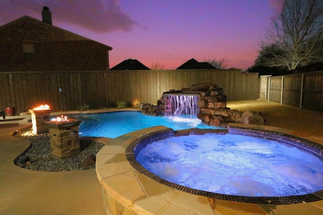 pool at dusk with a fenced in pool, an outdoor fire pit, a fenced backyard, and an in ground hot tub