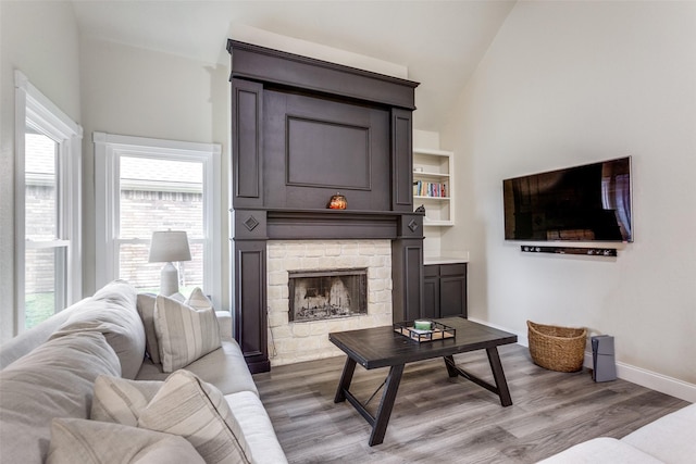 living room featuring wood-type flooring, lofted ceiling, and a stone fireplace