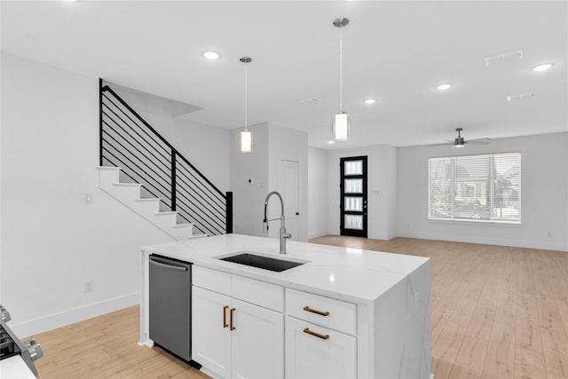 kitchen with stainless steel dishwasher, sink, white cabinetry, and light stone countertops