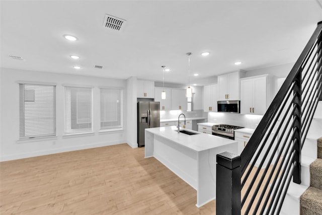 kitchen with a center island with sink, light wood-type flooring, white cabinetry, stainless steel appliances, and hanging light fixtures