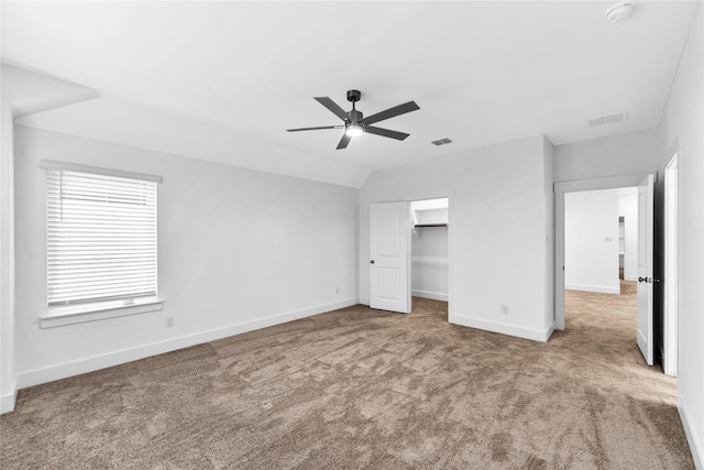 unfurnished bedroom with a closet, vaulted ceiling, a spacious closet, ceiling fan, and light colored carpet