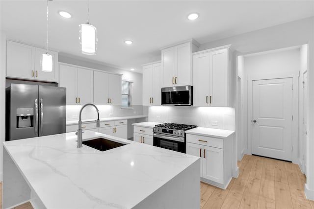 kitchen featuring appliances with stainless steel finishes, sink, pendant lighting, and a kitchen island with sink