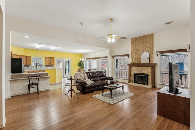 living area featuring ceiling fan, a brick fireplace, plenty of natural light, wood finished floors, and visible vents