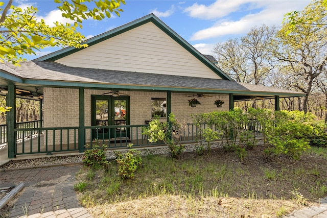 exterior space with a shingled roof, ceiling fan, a porch, and brick siding