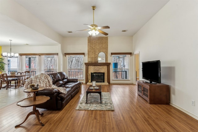 living area featuring visible vents, wood finished floors, ceiling fan with notable chandelier, and a fireplace