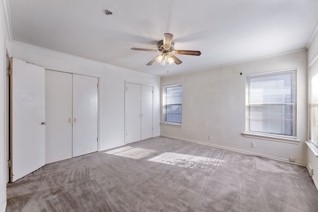 unfurnished bedroom with crown molding, two closets, light colored carpet, and ceiling fan