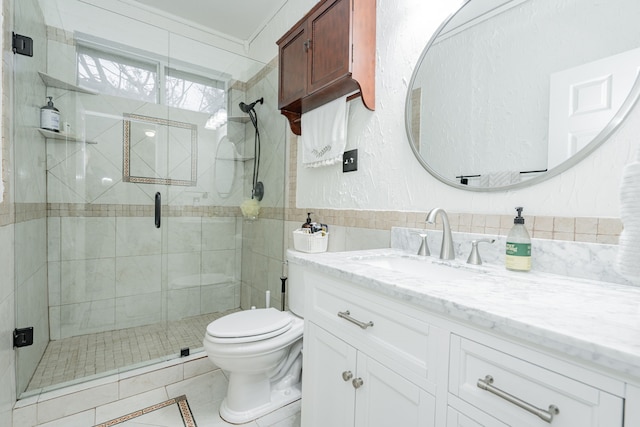 bathroom with a shower with shower door, tile walls, vanity, toilet, and tile patterned floors