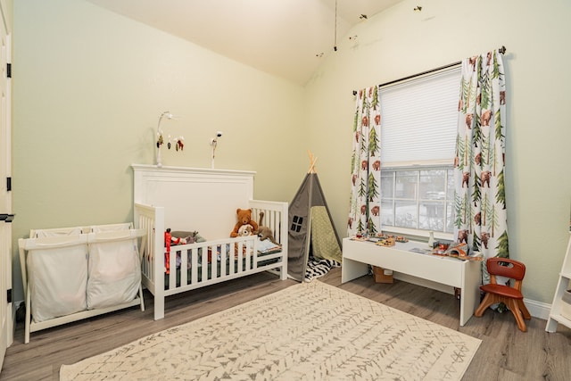 bedroom featuring vaulted ceiling, hardwood / wood-style floors, and a nursery area