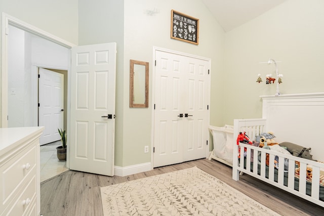 bedroom featuring high vaulted ceiling, light hardwood / wood-style flooring, and a nursery area